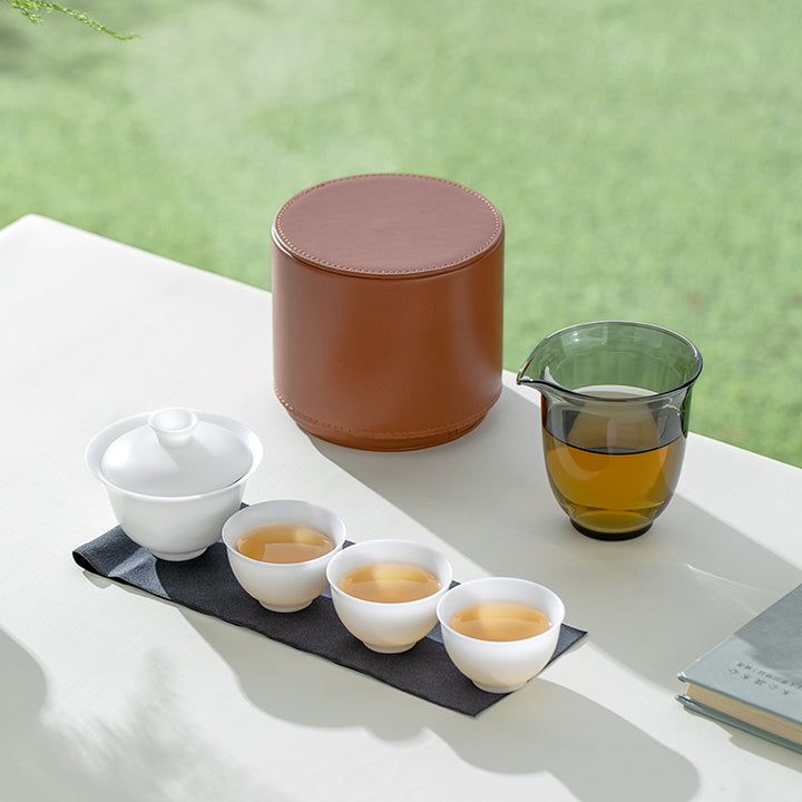Tea set with white teacups and a brown case on a white surface with a green background.