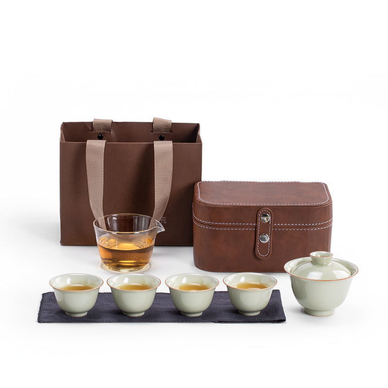 Tea set with ceramic cups, a glass teapot, and a brown carrying case on a white background.