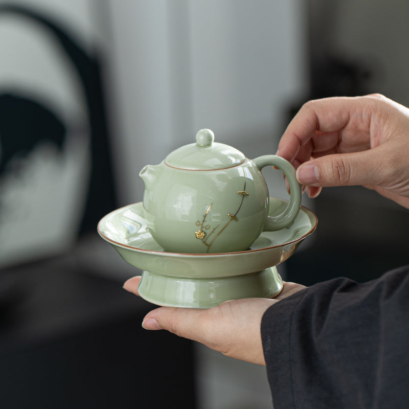 Person holding a green ceramic teapot with lid and tray