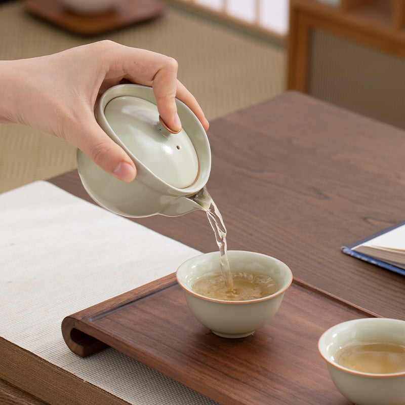 Person pouring tea from a teapot into a cup on a wooden table.