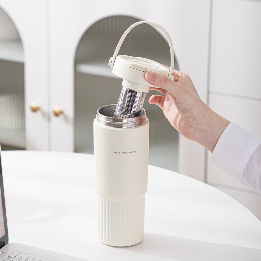 White travel mug with a filter being held by a hand in a kitchen setting.