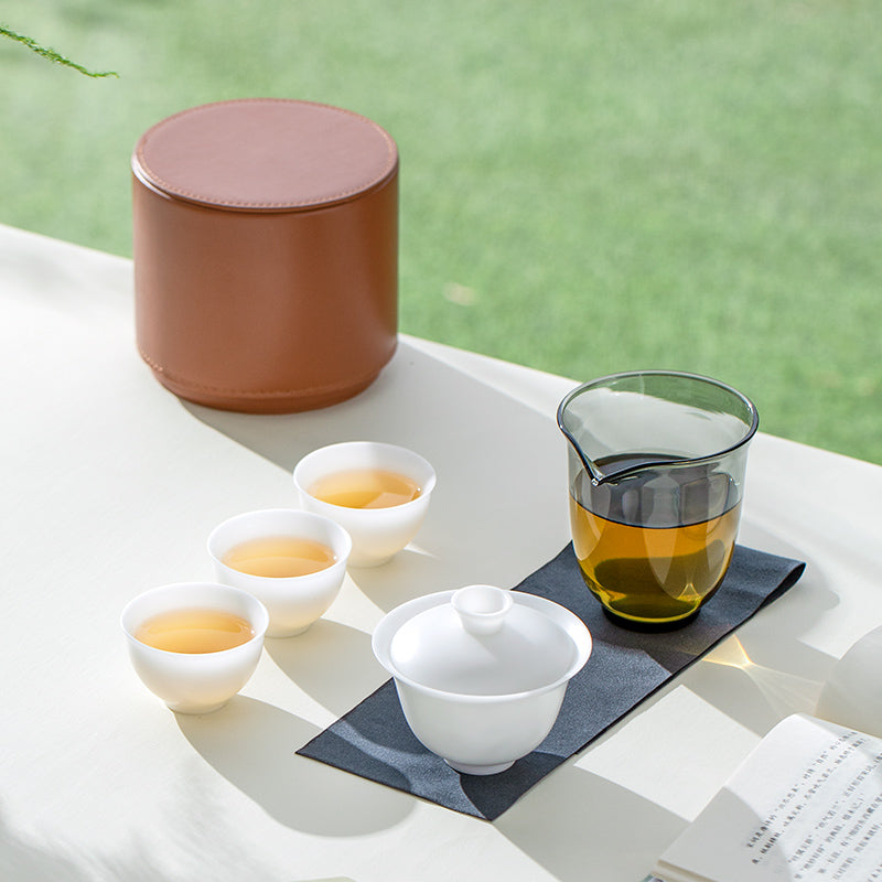 white gaiwan tea set with ceramic container, glass pitcher, and white teacups on a table with a blurred natural background.