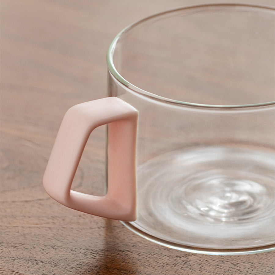 Clear glass mug with a pink handle on a wooden surface