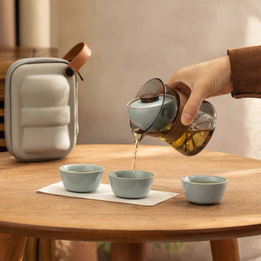 Person pouring tea from a glass teapot into small ceramic cups on a wooden table.