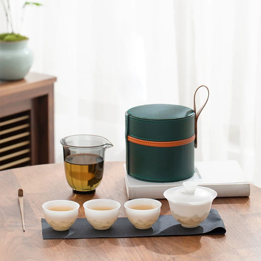 Tea set with green container, glass teapot, and ceramic cups on a wooden table.