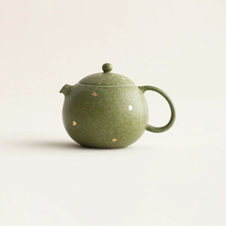 Green ceramic teapot with speckled pattern on a light beige background