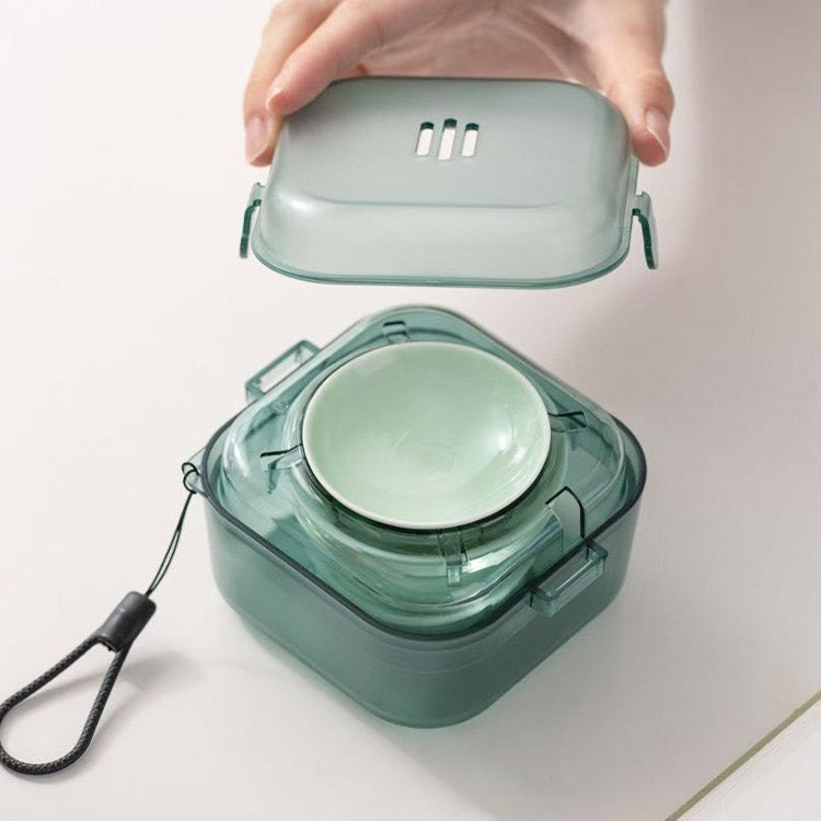 A translucent mint green portable container with a matching inner bowl and a hand lifting the lid, shown on a clean white surface.