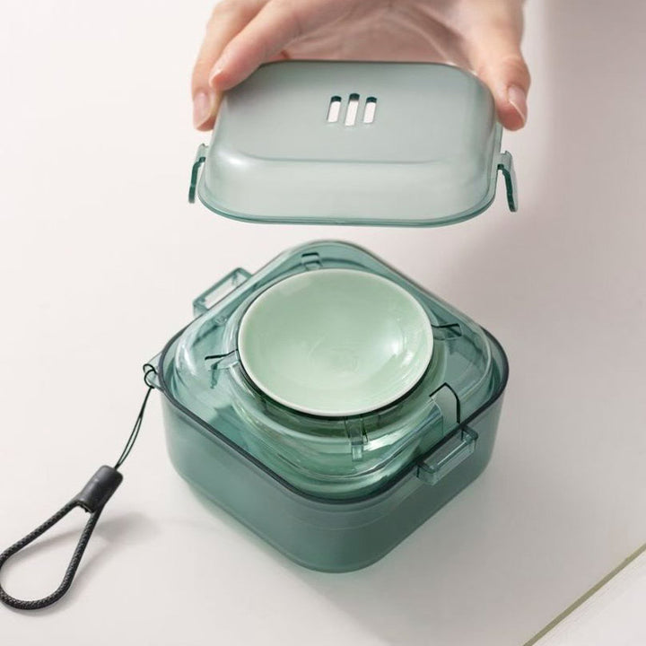 A translucent mint green portable container with a matching inner bowl and a hand lifting the lid, shown on a clean white surface.