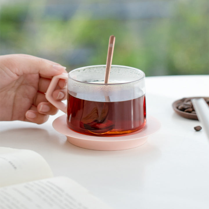 Glass mug with a pink base filled with tea, held by a hand on a blurred natural background.