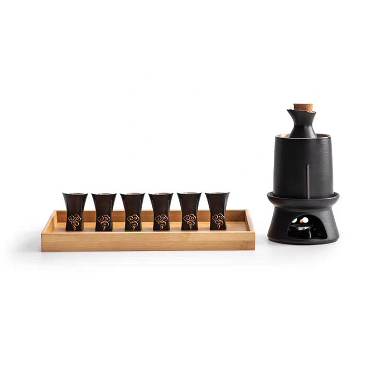 A ceramic sake set on a white background, featuring a black ceramic sake holder with a cork stopper on a black base, and six matching small black cups arranged in a light natural bamboo tray.