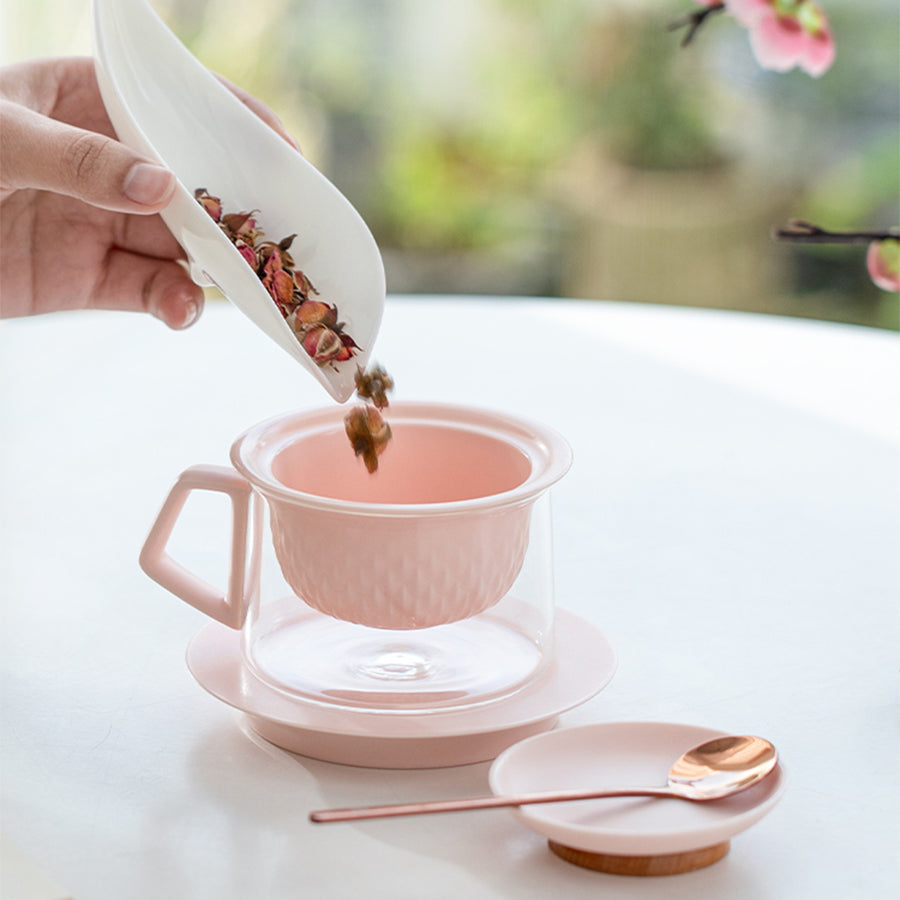 Person adding tea leaves to a pink teacup with a white background