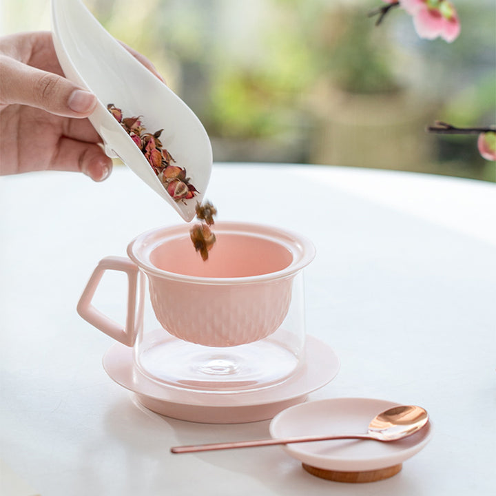 Person adding tea leaves to a pink teacup with a white background