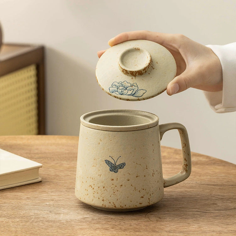 Ceramic mug with lid featuring butterfly design on a wooden table.