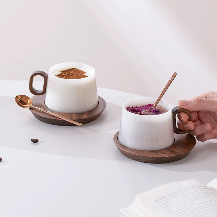 Two white mugs with wooden handles on wooden saucers, one filled with a brown substance and the other with a pink substance, on a light surface.