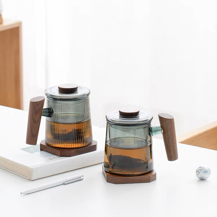 A custom glass tea mug with a walnut wood saucer and a white product packaging box, set against a neutral background.